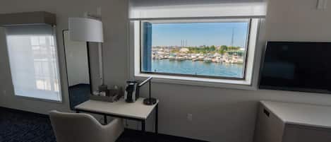 A hotel room with a desk, chair, TV, and a window with a marina view.