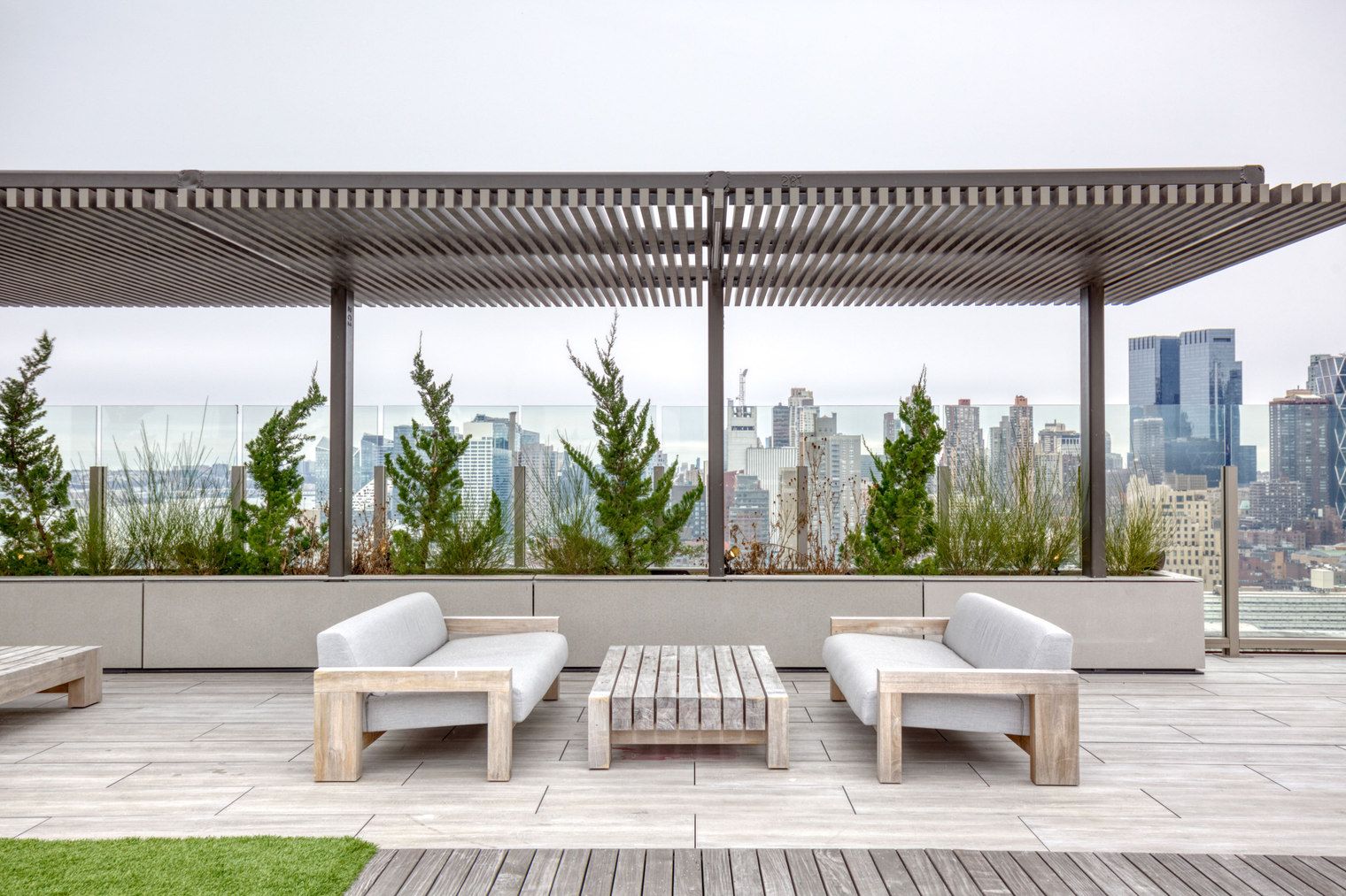 A rooftop patio with two white sofas, a wooden table, and a pergola.