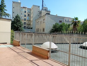 A rooftop terrace with a metal fence, a brick wall, and a view of surrounding buildings.