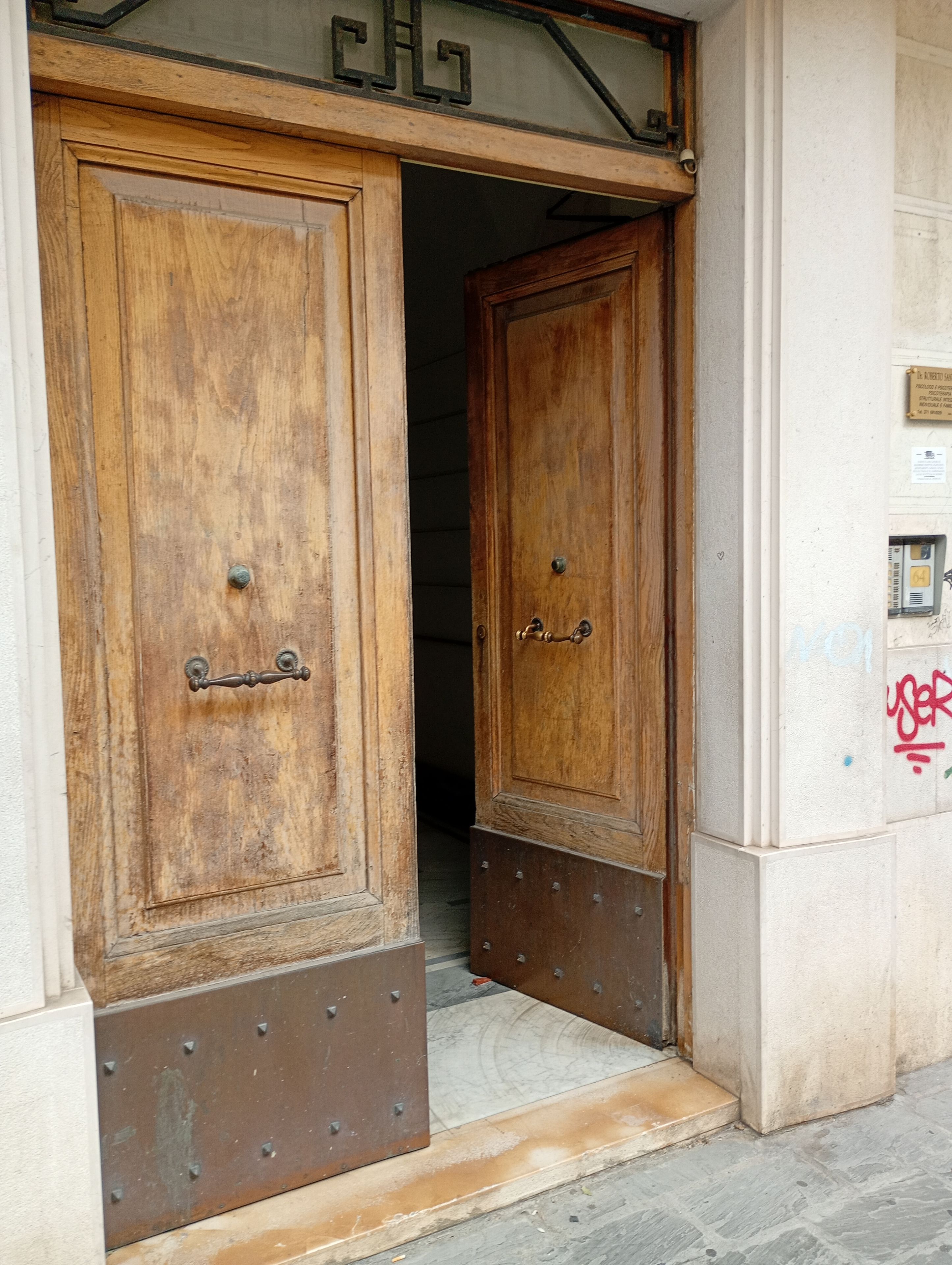 Puerta doble de madera con base de metal, que da a un pasillo con suelo de baldosas.