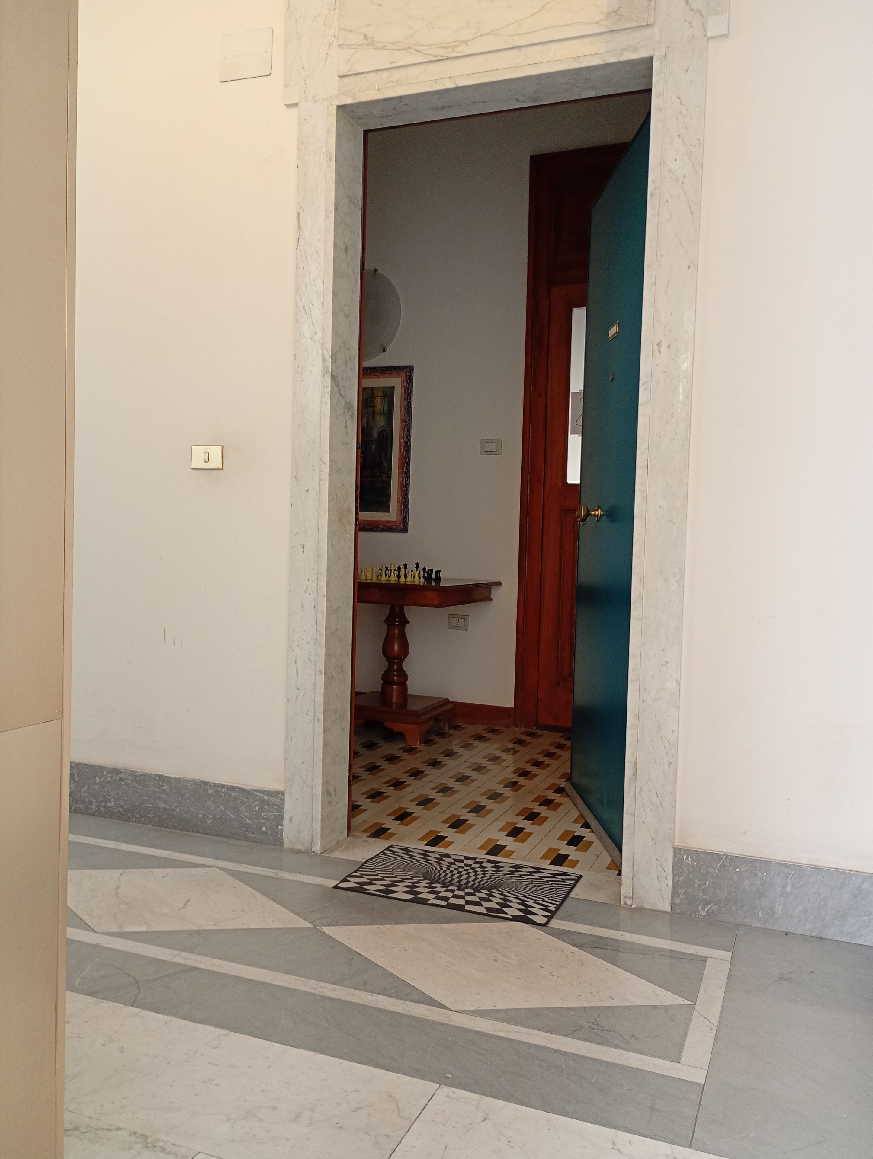 Un pasillo con piso estampado, un tablero de ajedrez y una puerta que da a otra habitación.