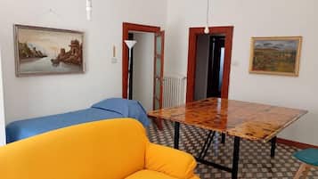 Una habitación con suelo a cuadros, una mesa de madera, un sofá amarillo y dos puertas que dan a otras habitaciones.
