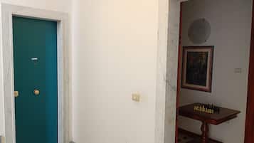 Un couloir avec une porte de couleur turquoise, un mur en marbre, un tableau encadré et un jeu d’échecs posé sur une table en bois.