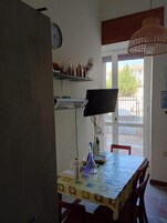 A dining area with a table, chairs, a clock, a television, and a window with a view of the outside.