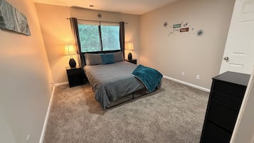 A bedroom with a bed, two bedside tables with lamps, a window with curtains, a door, and a wall with decorative stickers.