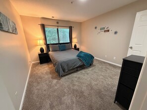 A bedroom with a bed, two bedside tables with lamps, a window with curtains, a door, and a wall with decorative stickers. -  The Nestled Oasis ~ Free Parking ~ Minutes to Duke/Downtown (Durham)