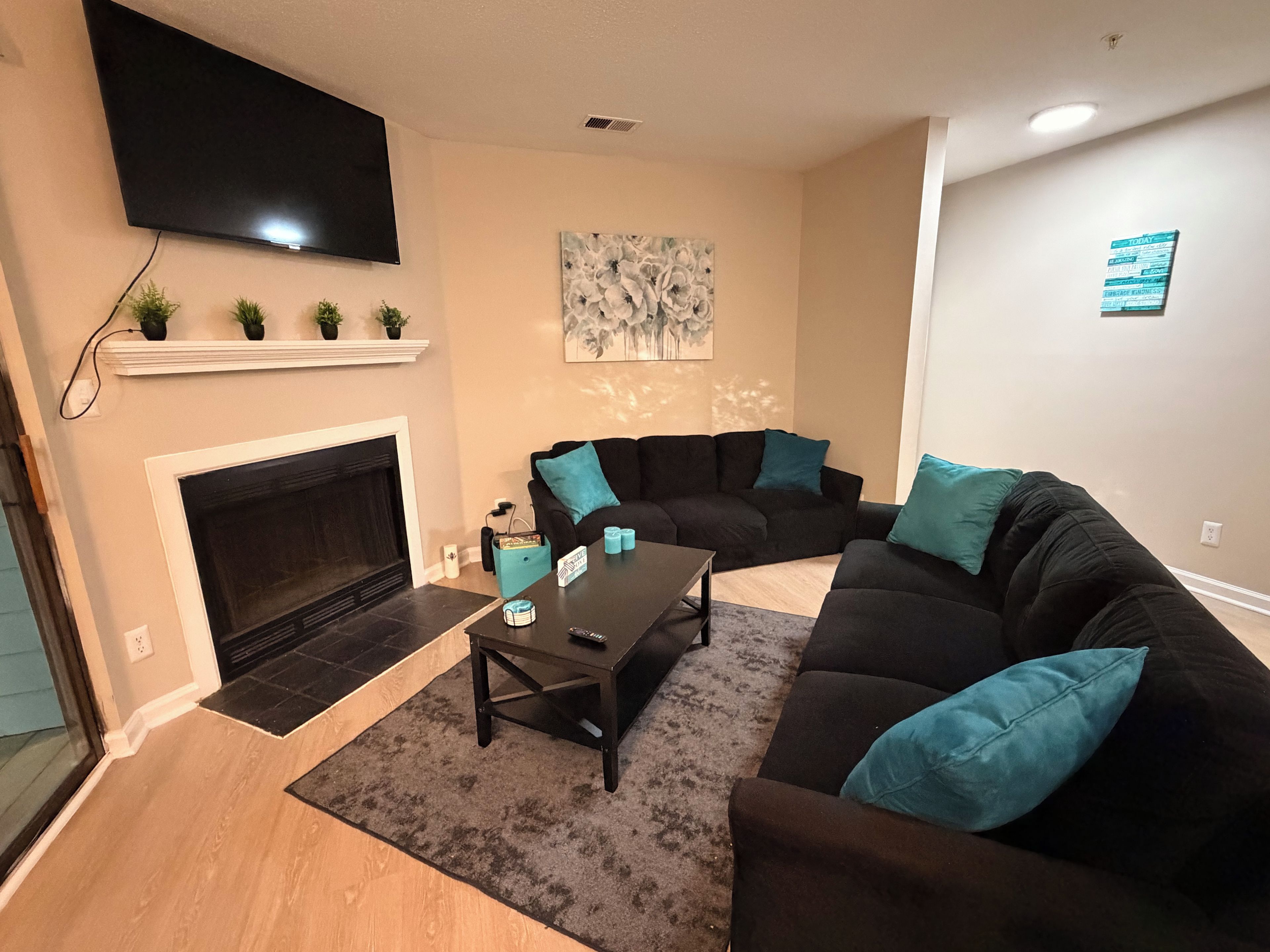 A living room with a fireplace, a black sofa, a coffee table, and a flat-screen TV mounted on the wall.
