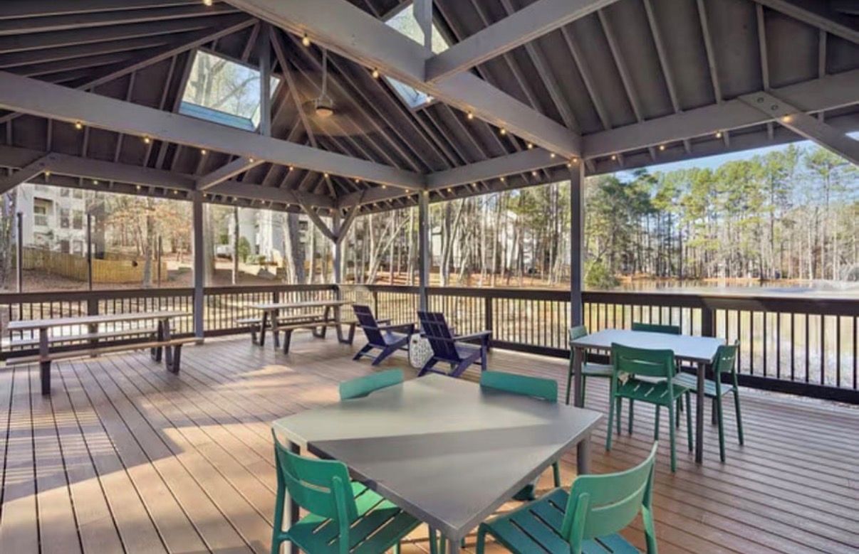 Une terrasse extérieure couverte, dotée de tables et de chaises, ainsi qu’une plateforme en bois, le tout offrant une vue sur une zone boisée.