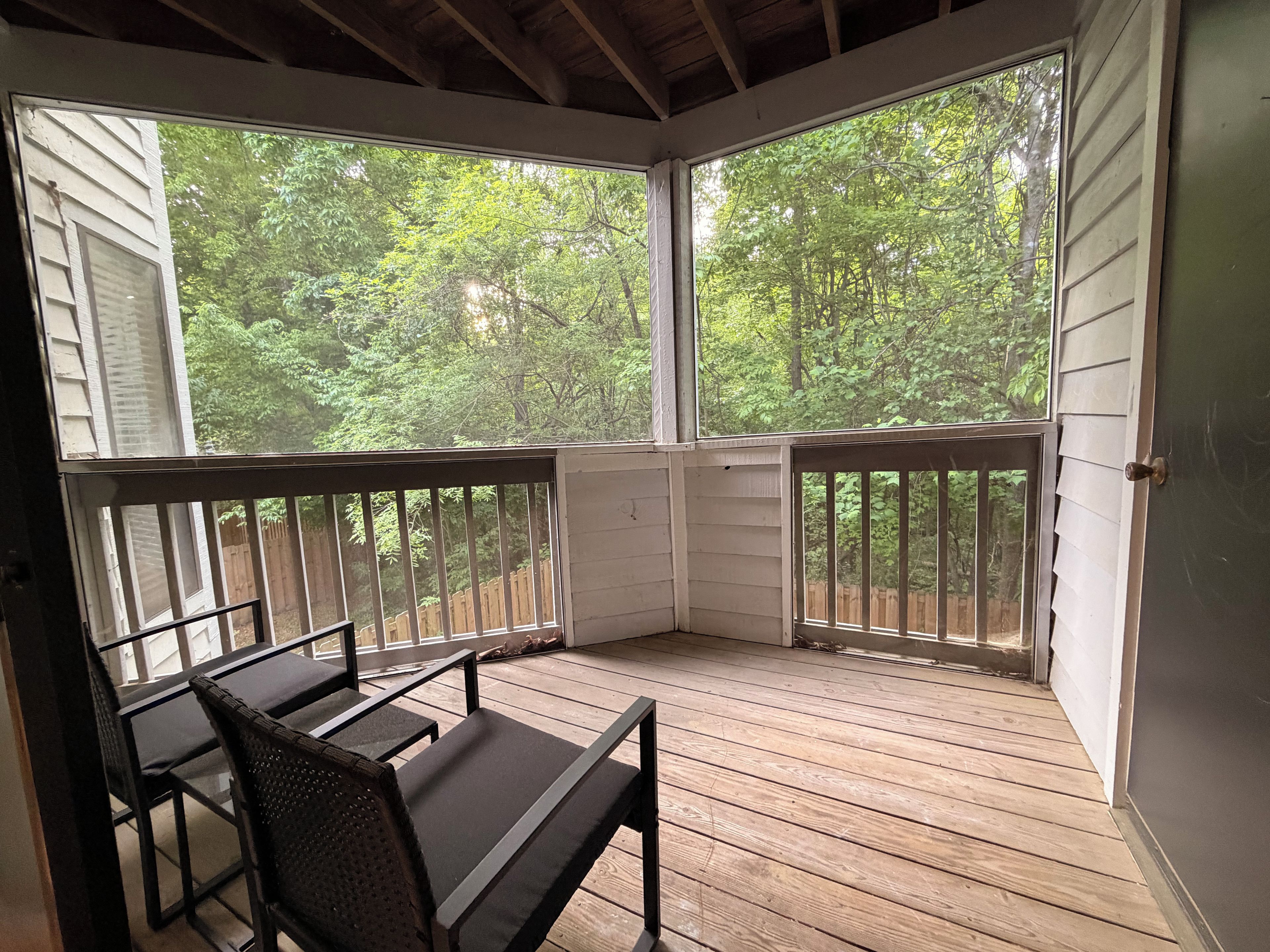 A covered outdoor area with a wooden deck, a table, and two chairs.