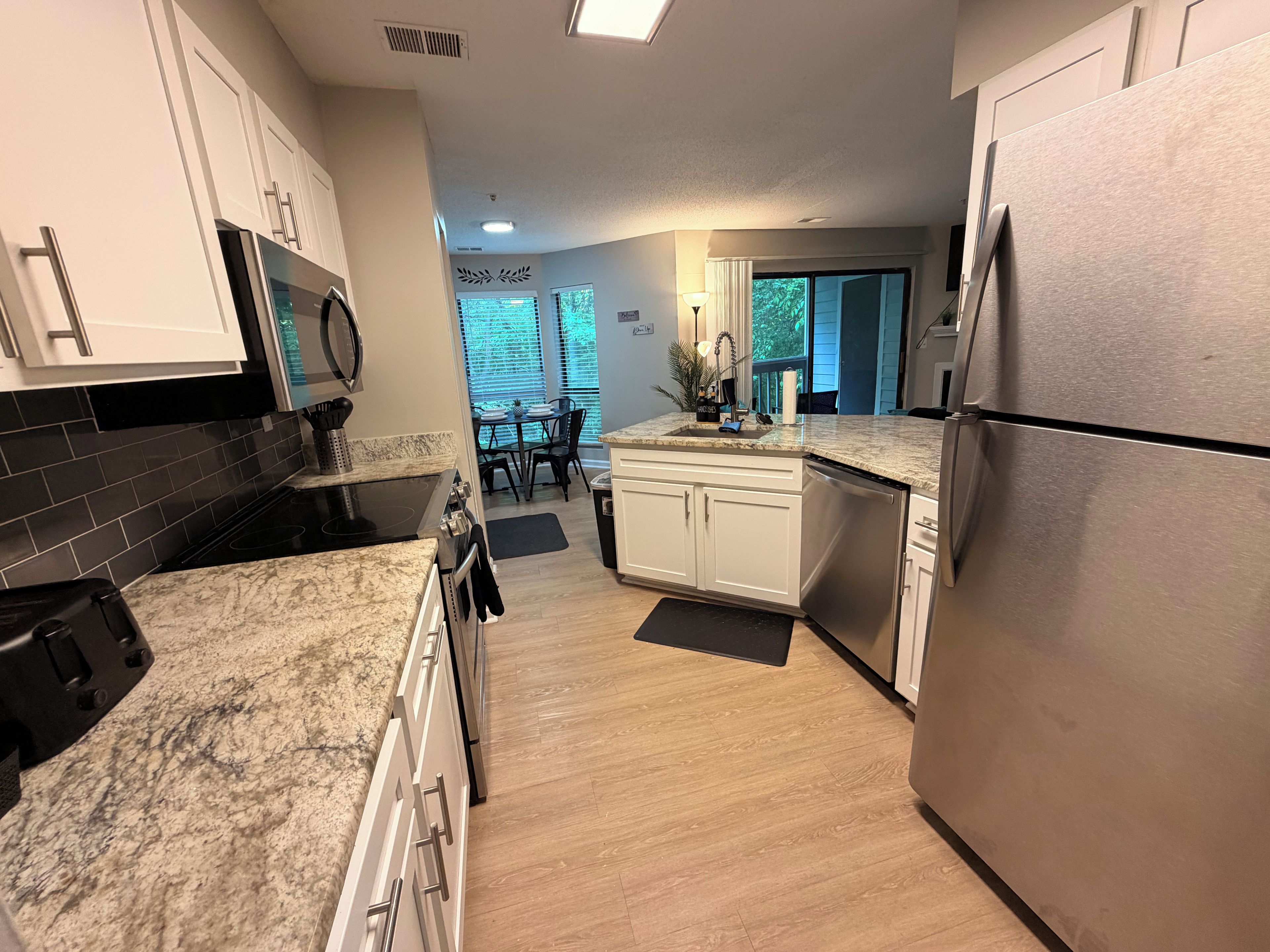 A modern kitchen with white cabinets, a stainless steel refrigerator, and a black tiled backsplash.
