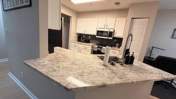 A modern kitchen with white cabinets, a granite countertop, and a welcome sign.