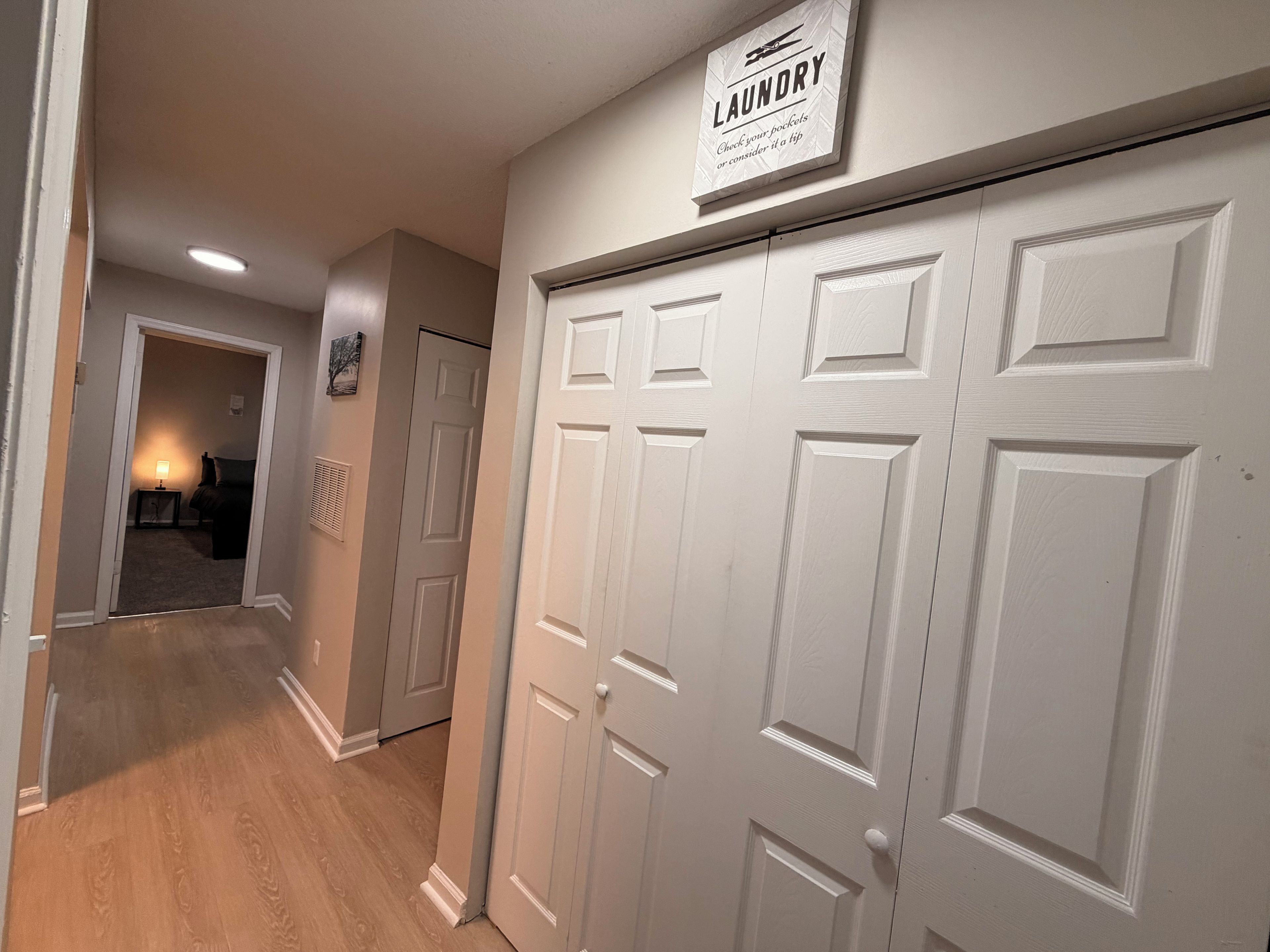 A hallway with a laundry sign, a closed door, and a lamp in the background.
