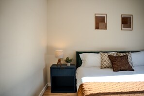 Une chambre à coucher avec un lit, une table de chevet, une lampe et deux tableaux encadrés accrochés au mur.