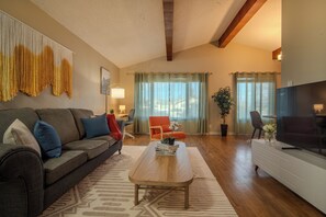 A living room with a sofa, coffee table, and TV. There is a window with curtains, a plant, and a lamp. - Bright Family Home | 10 mins to Airport & Downtown (Calgary)