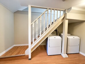 A staircase with a white railing leading to a laundry area with two white washing machines. - Bright Family Home | 10 mins to Airport & Downtown (Calgary)