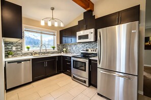 A modern kitchen with dark cabinetry, stainless steel appliances, a microwave, oven, and a refrigerator. - Bright Family Home | 10 mins to Airport & Downtown (Calgary)