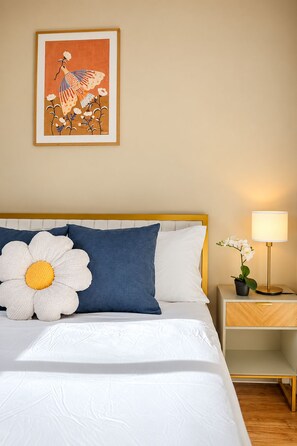 A neatly made bed with a large flower pillow, a bedside table with a lamp, and a framed artwork above the bed. - Bright Family Home | 10 mins to Airport & Downtown (Calgary)