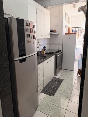 A compact kitchen with a stainless steel refrigerator, white cabinets, a gas stove, and a tiled floor.