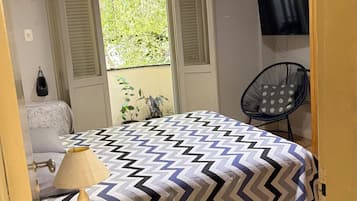Quarto com cama, poltrona, televisão e janela com persianas.