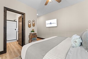 Een slaapkamer met een bed, een dressoir, een spiegel en een wandtelevisie waarop RENTBRLNSON.COM wordt weergegeven.