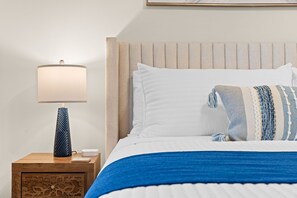 A neatly made bed with a blue blanket, a white pillow, and a striped throw pillow. There is a wooden nightstand with a lamp and a device beside it. - Near Outdoor Pool&Lazy River_Free Attraction Tickets_Private Hot Tub_Kids Room (Hollister)