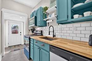 A kitchen with teal cabinets, a wooden countertop, a built-in oven, and a dishwasher. - Roadmap Lodging: Craftsman 3BR, Near Downtown Indy (Indianapolis)