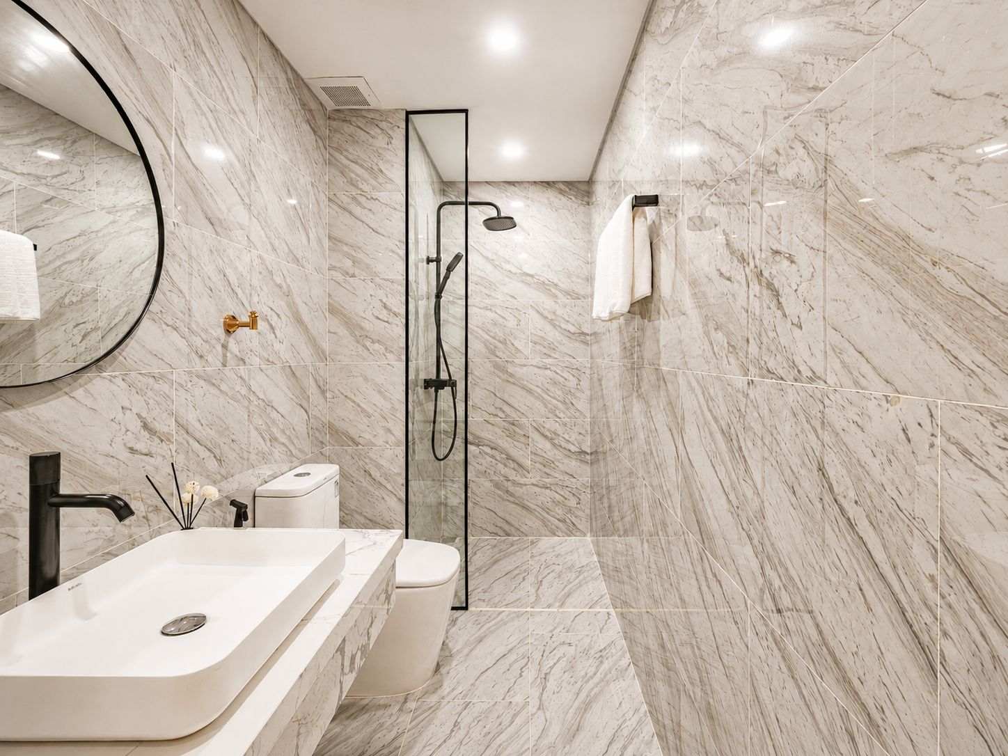 A modern bathroom with a marble floor, a glass-enclosed shower, a white sink, and a toilet.