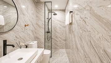 A modern bathroom with a marble floor, a glass-enclosed shower, a white sink, and a toilet.