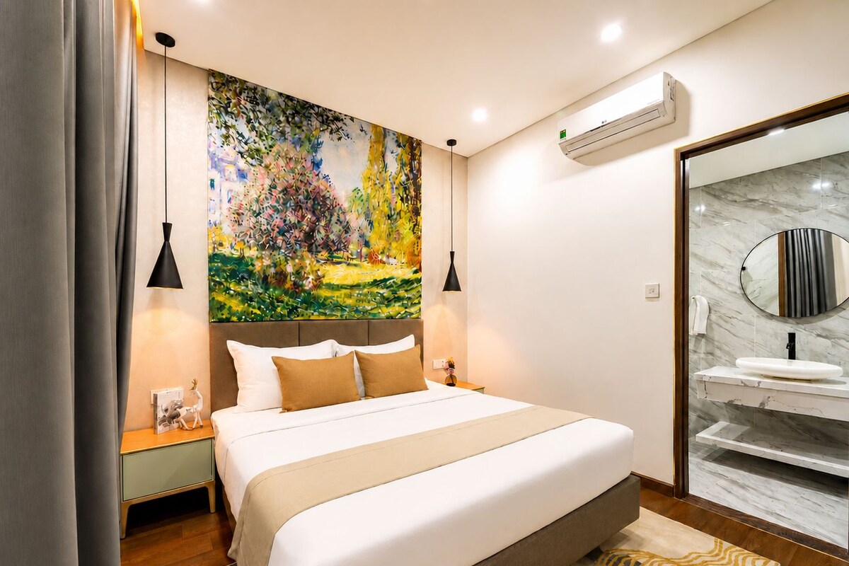 Une chambre d’hôtel moderne avec un grand lit, un tableau au-dessus de la tête de lit, une salle de bain dotée d’un comptoir en marbre et un appareil de climatisation fixé au mur.