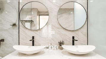 Une salle de bain avec deux lavabos, une douche et un miroir au-dessus des lavabos.