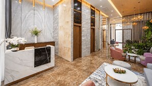Zona d'entrada moderna amb parets de marbre, una taquilla d'hostal i un espai d'estar amb sofàs i una taula de cafè.