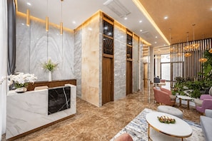 Un espace d’accueil moderne avec des murs en marbre, un comptoir d’accueil et un coin salon comprenant des canapés et une table basse.