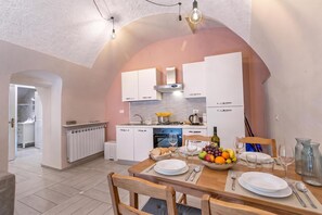A modern kitchen with white cabinets, a built-in oven, and a dining area with a wooden table set for two. - Icardi 2 Casa Di Mattoni, Dolceacqua, Italy (Dolceacqua)