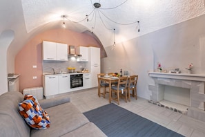 A modern kitchen with white cabinets, a built-in oven, and a dining area with wooden chairs and a table. - Icardi 2 Casa Di Mattoni, Dolceacqua, Italy (Dolceacqua)