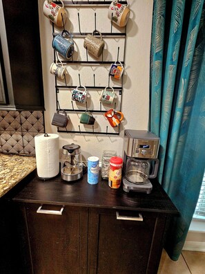 A kitchen counter with a coffee maker, paper towels, a container of granola, and a jar of coffee creamer.