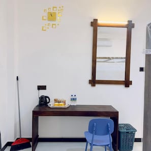 A room with a wooden desk, a blue chair, a wall clock, a mirror, and a broom.
