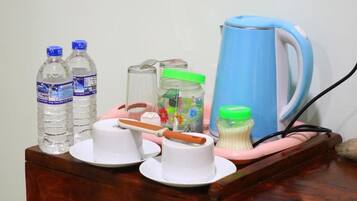 A wooden table with a blue kettle, two water bottles, a jar with a green lid, a white cup, and a white plate with a spoon.