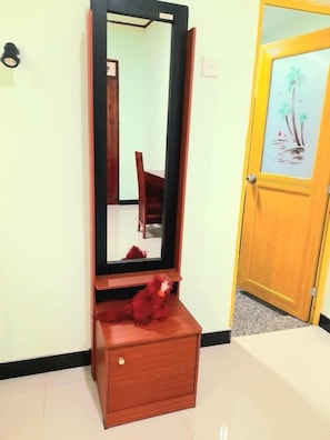 A wooden dresser with a mirror, a red plush toy on top, and a door with a glass panel and artwork.