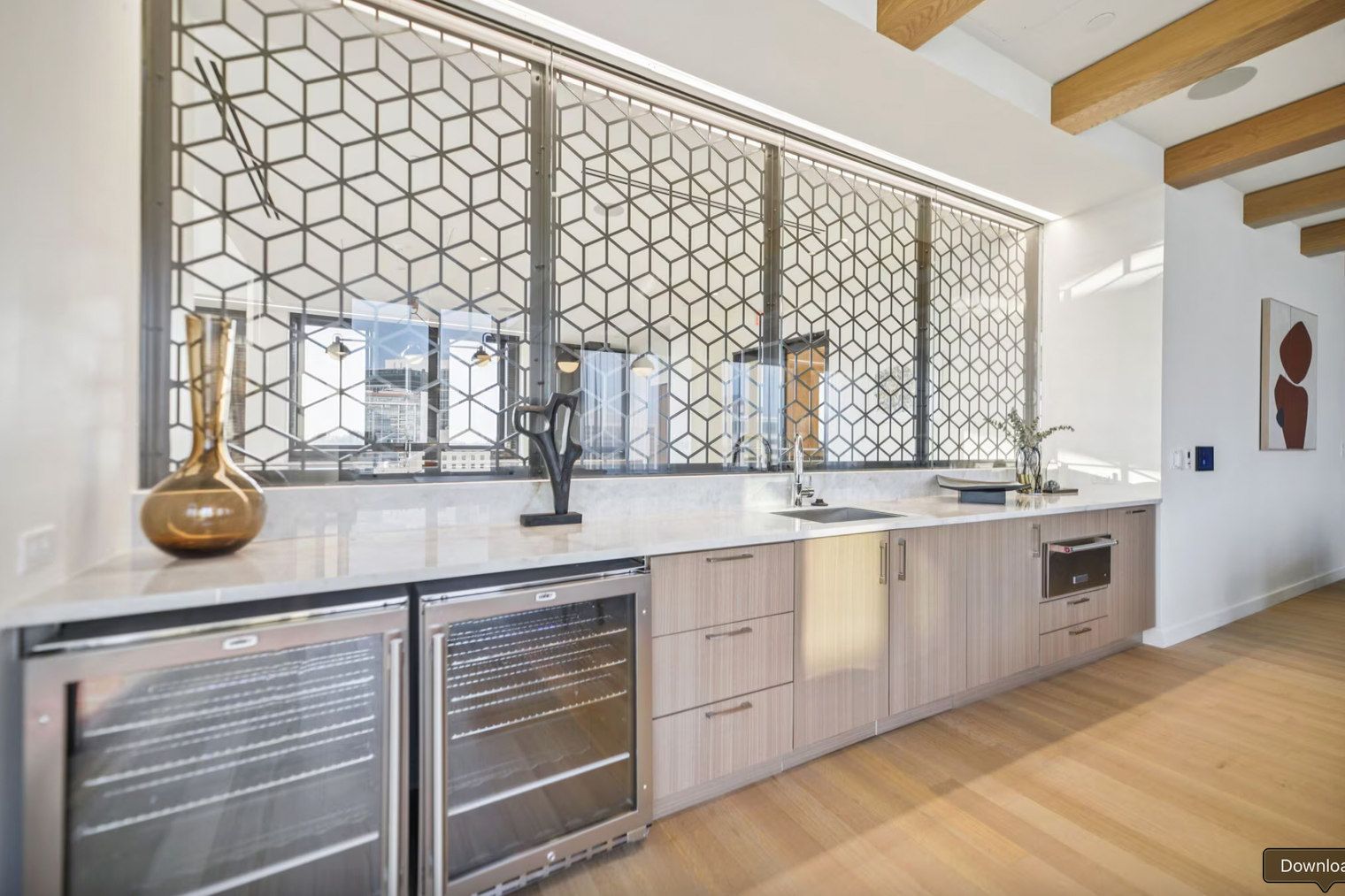 Una cocina moderna con un ventanal grande, hornos integrados y un panel metálico decorativo.