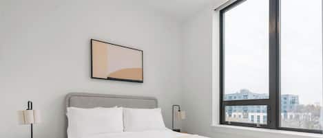 Habitación de hotel con cama, ventana y una obra de arte abstracta colgada en la pared.