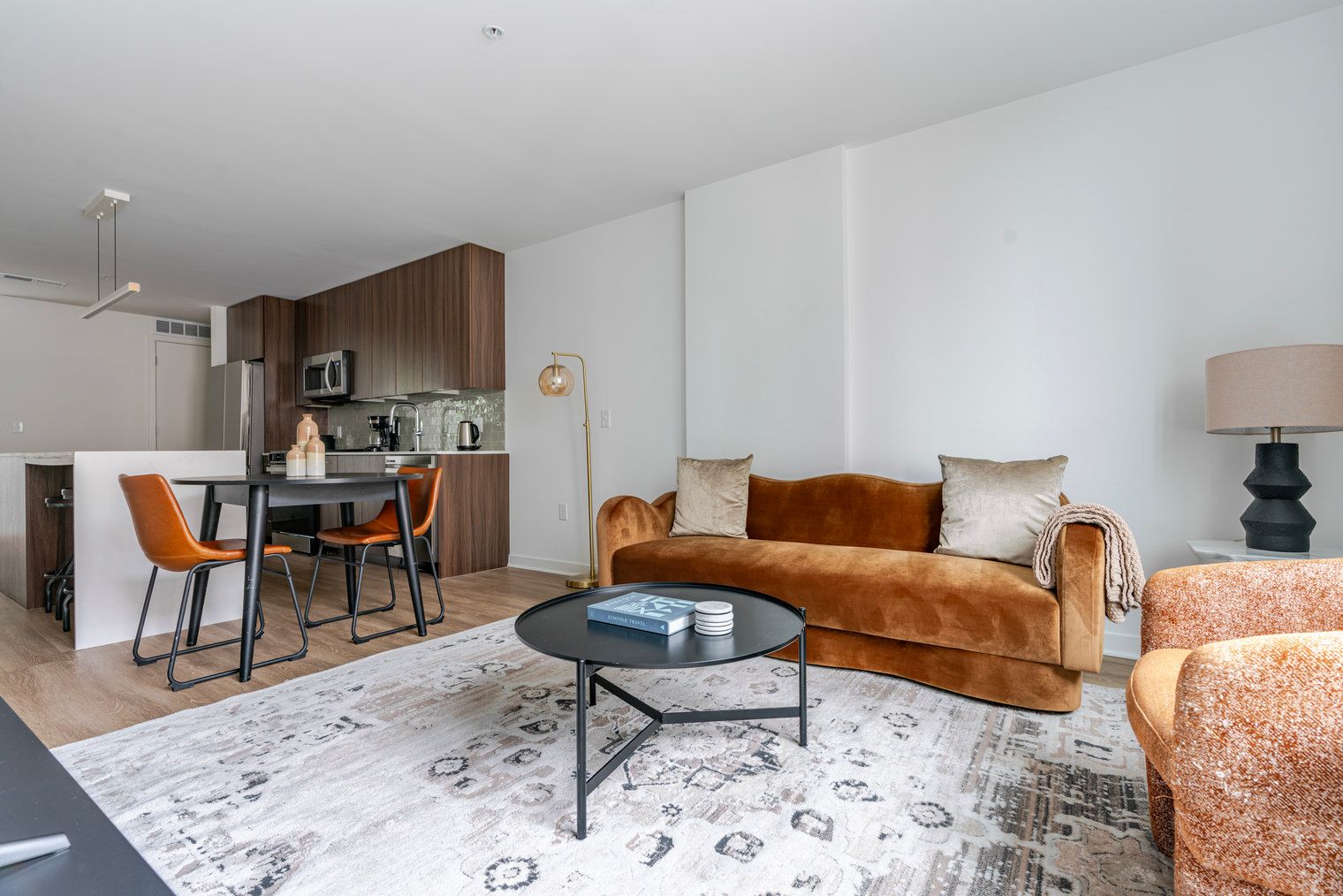 Un salon moderne avec un canapé, une table basse et des fauteuils. Il y a également un coin cuisine avec une table à manger et des chaises.