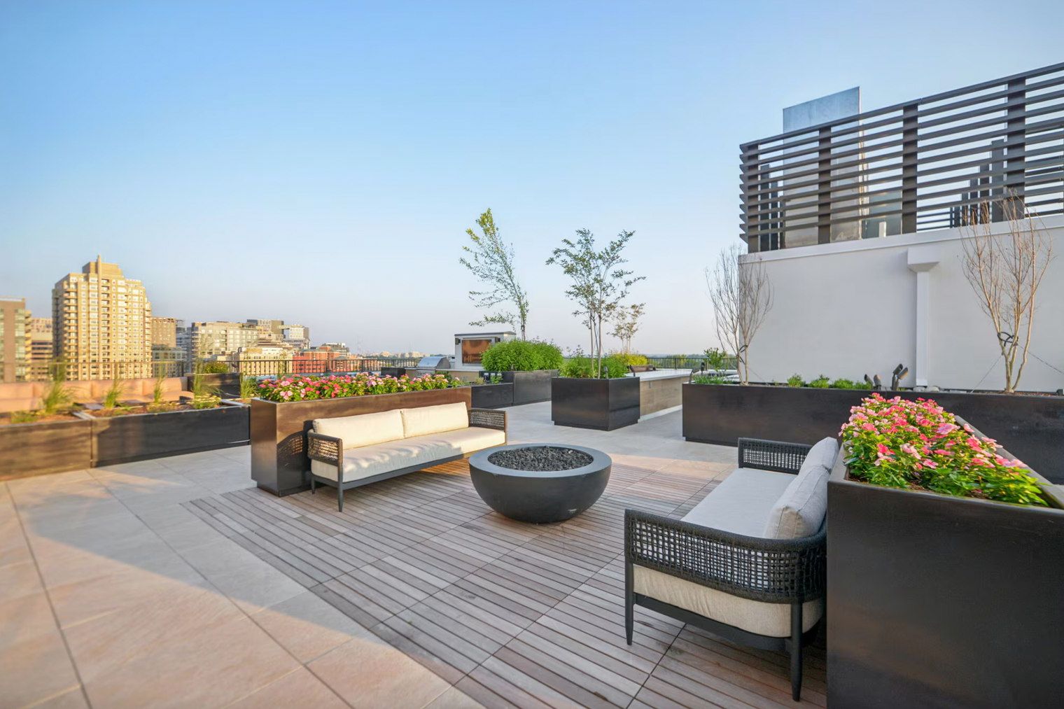 Eine Dachterrasse mit Sitzgelegenheiten, Pflanzgefäßen und Blick auf die Stadtlandschaft.