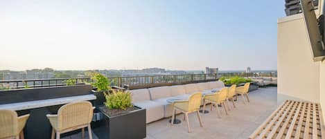 Una terraza en la azotea con sofá, sillas y macetas.