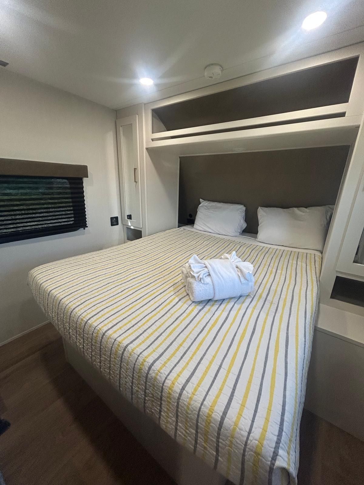 A single bed with a striped bedspread, a folded towel, and a headboard.