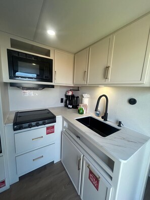 Bright modern kitchenette with cooktop, microwave, and farmhouse sink