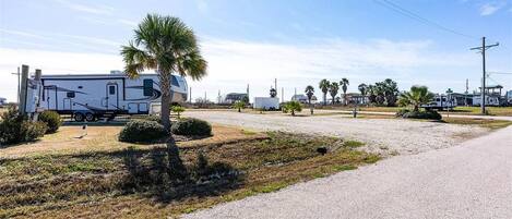 A gravel parking area with a white RV and a palm tree.