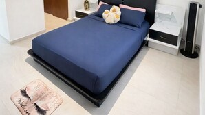 Une chambre à coucher avec un grand lit, une table de chevet, une commode, un téléviseur fixé au mur et une porte donnant sur une autre pièce.