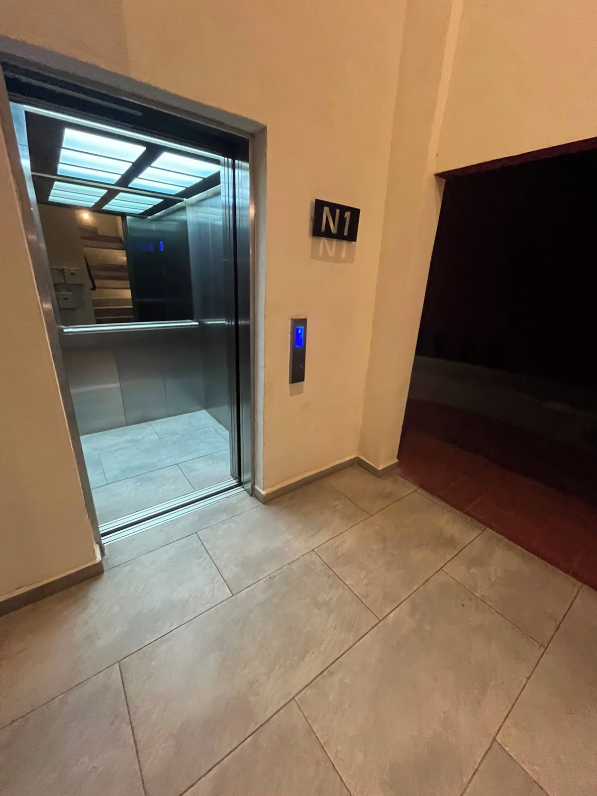 Un ascensor amb pantalla digital, sòl de rajoles i un senyal que indica 'N1'.