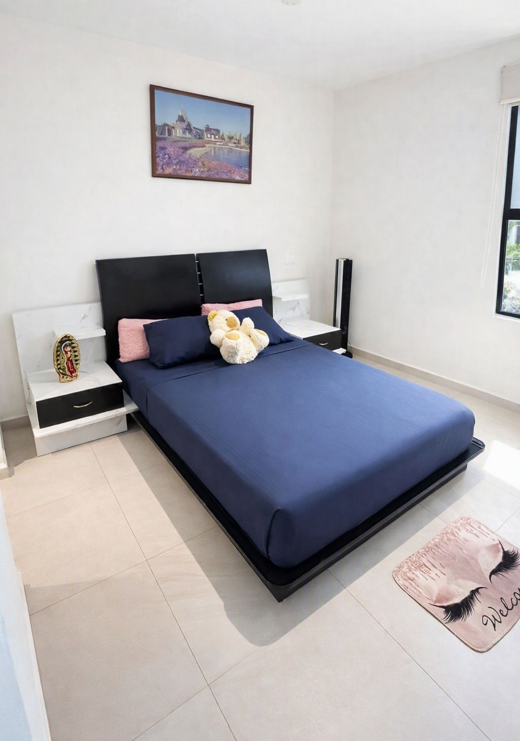 A bedroom with a bed, bedside tables, a nightstand, a wall-mounted TV, and a window.