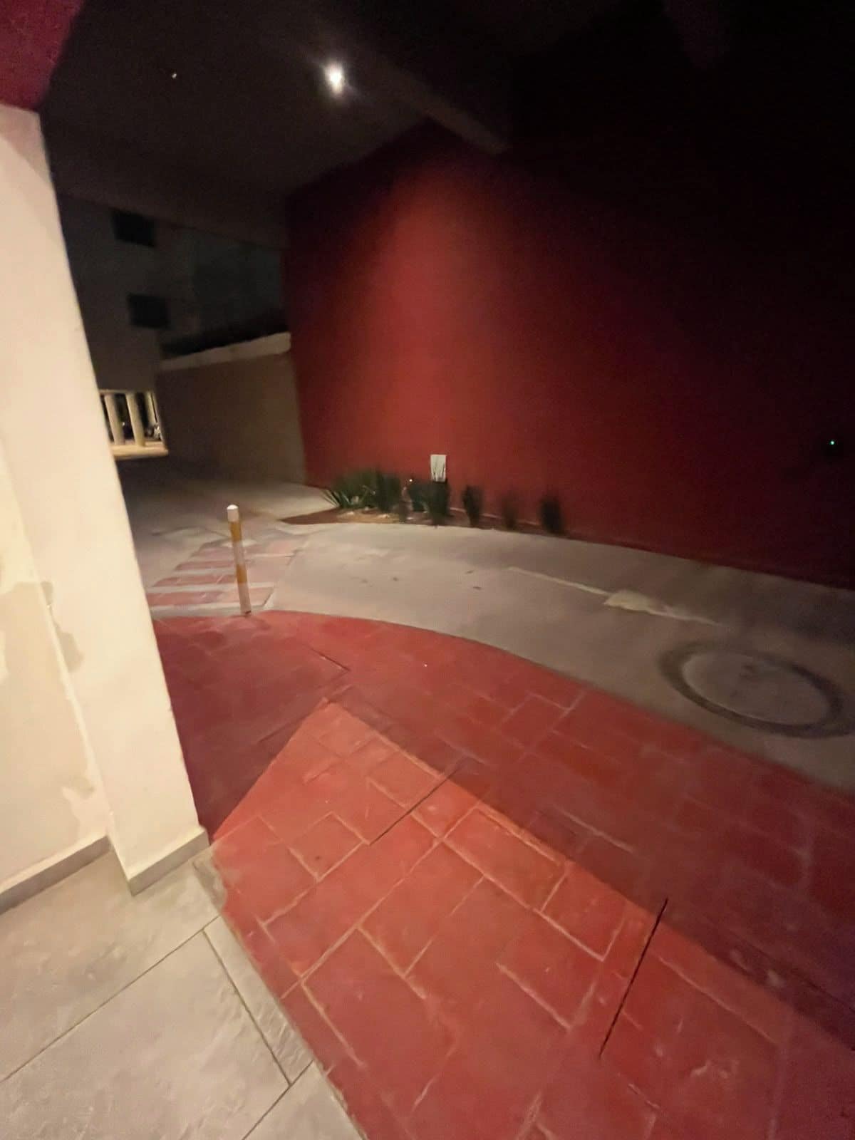 Área externa com pouca luz, parede vermelha e chão de azulejos.